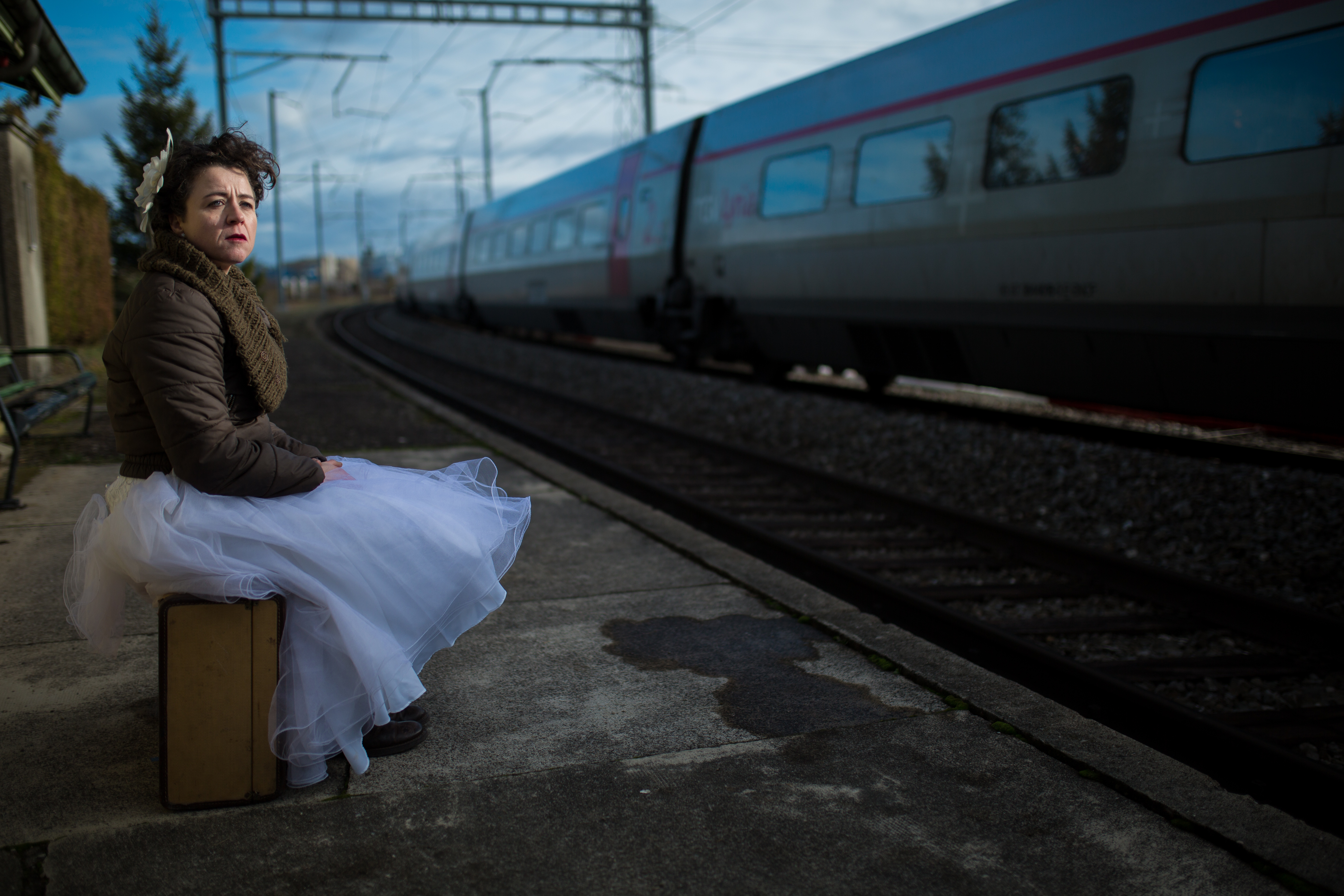 a woman in a wedding dress sits on a suitcase as a train passes